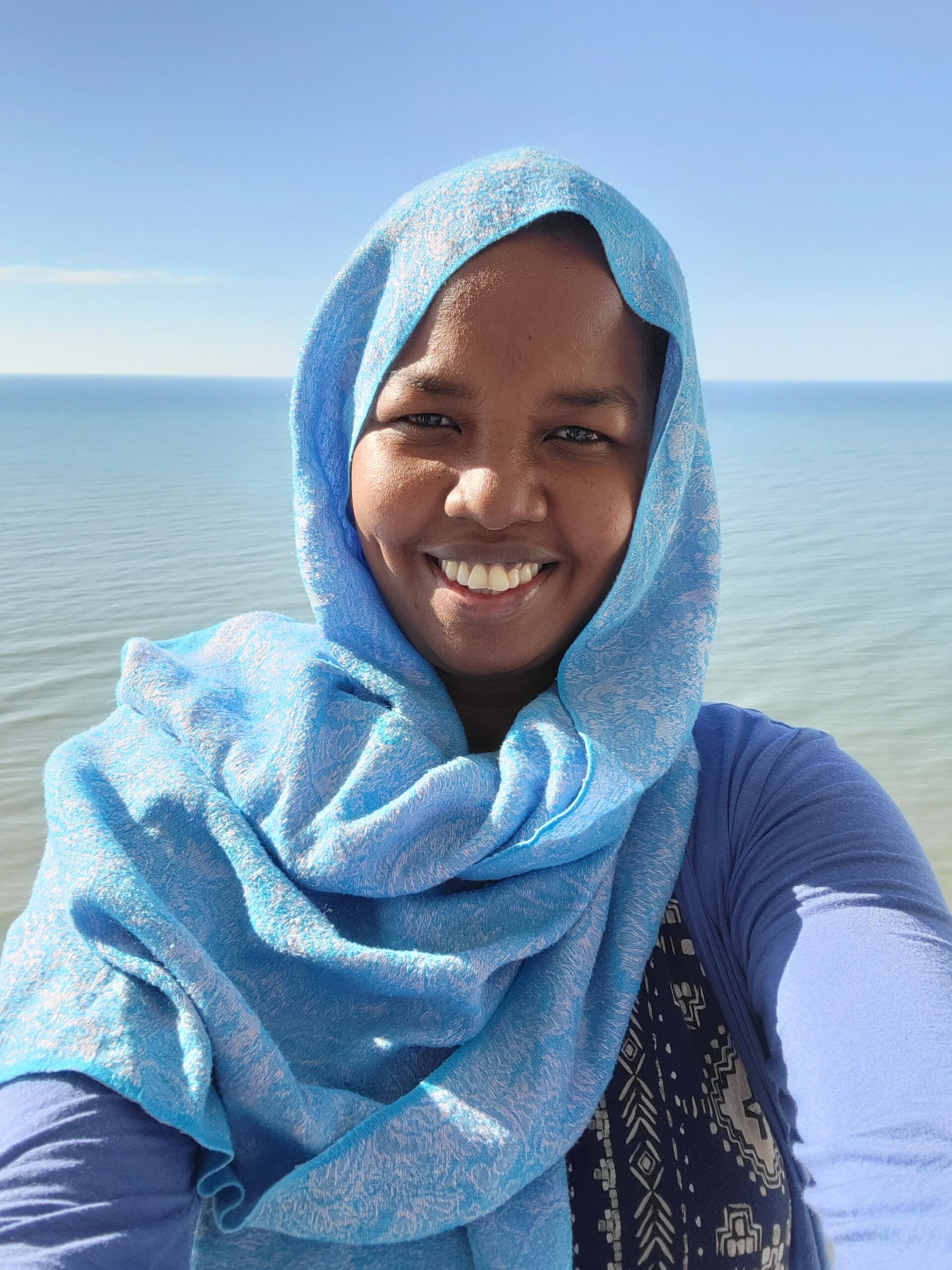 A Woman Wearing a Blue Hijab Smiles Warmly at the Camera.